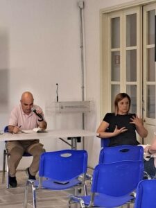 Η φωτογραφία δείχνει τον κ. Φίλιππο Παπαμιχαήλ να κρατάει το μικρόφωνο και να μοιράζεται την ιστορία του με τη σκλήρυνση κατά πλάκας. Δίπλα του η κυρία Παναγιώτα Θεμιστοκλέους μεταφράζει στη νοηματική γλώσσα.