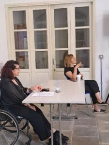 Η φωτογραφία δείχνει την κυρία Δέσποινα Ρούσου να μοιράζεται την ιστορία της με την κατά πλάκας σκλήρυνση . Δίπλα της η κυρία Παναγιώτα Θεμιστοκλέους μεταφράζει στη νοηματική γλώσσα.