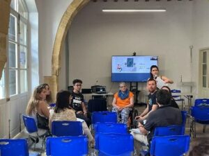 The photo shows a group of participants listening to a speaker.